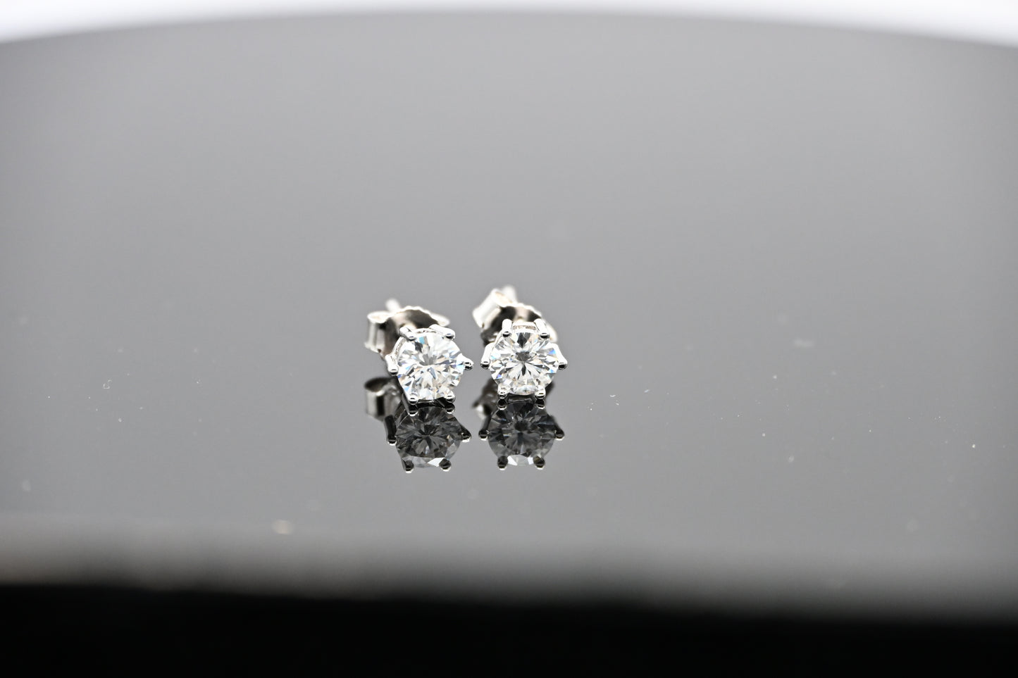 Pair of diamond stud earrings on a reflective surface