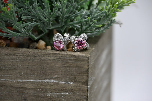 Pair of butterfly-shaped earrings with pink gemstones on a wooden surface with greenery in the background.
