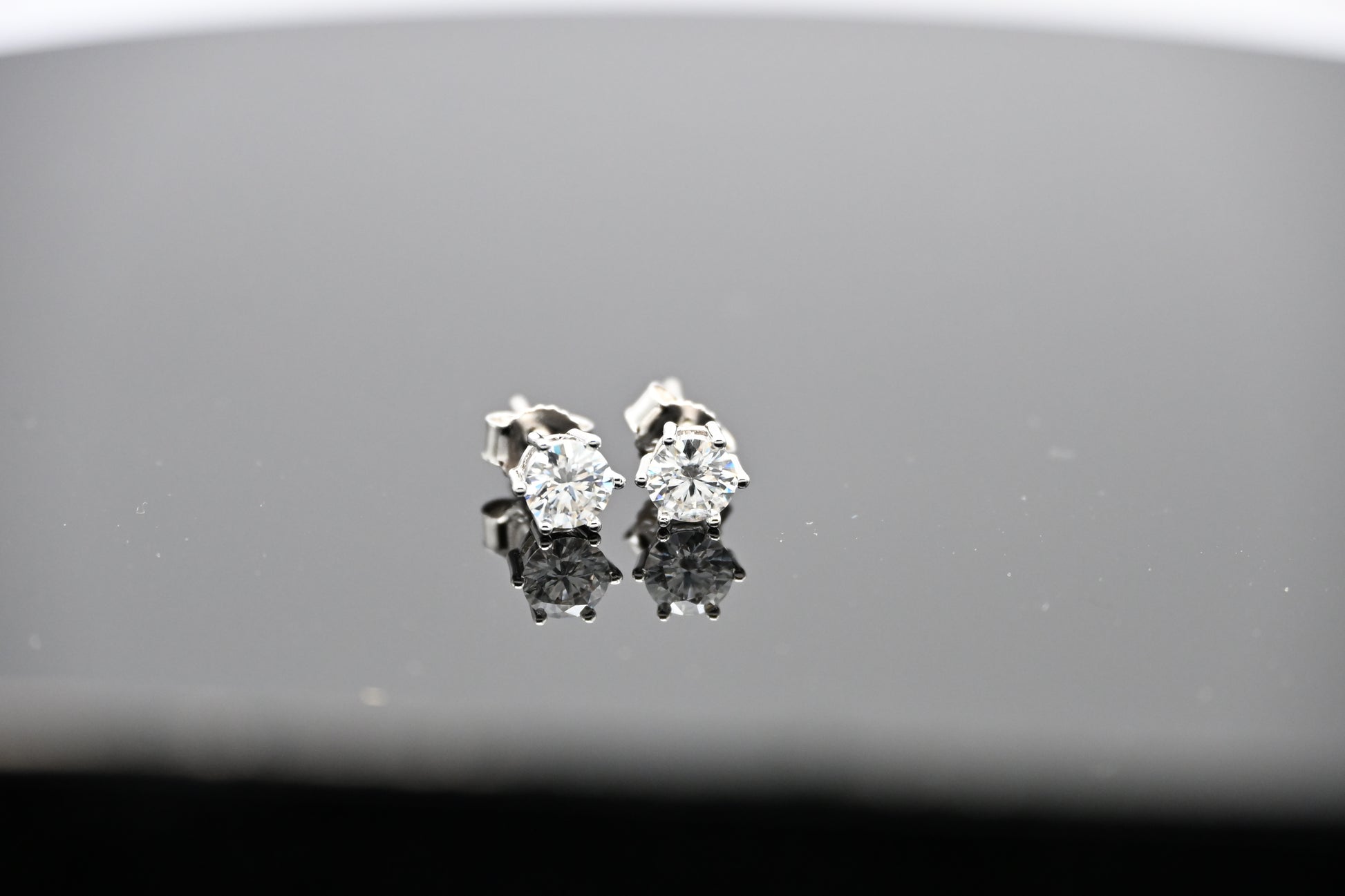 Pair of diamond stud earrings on a reflective surface